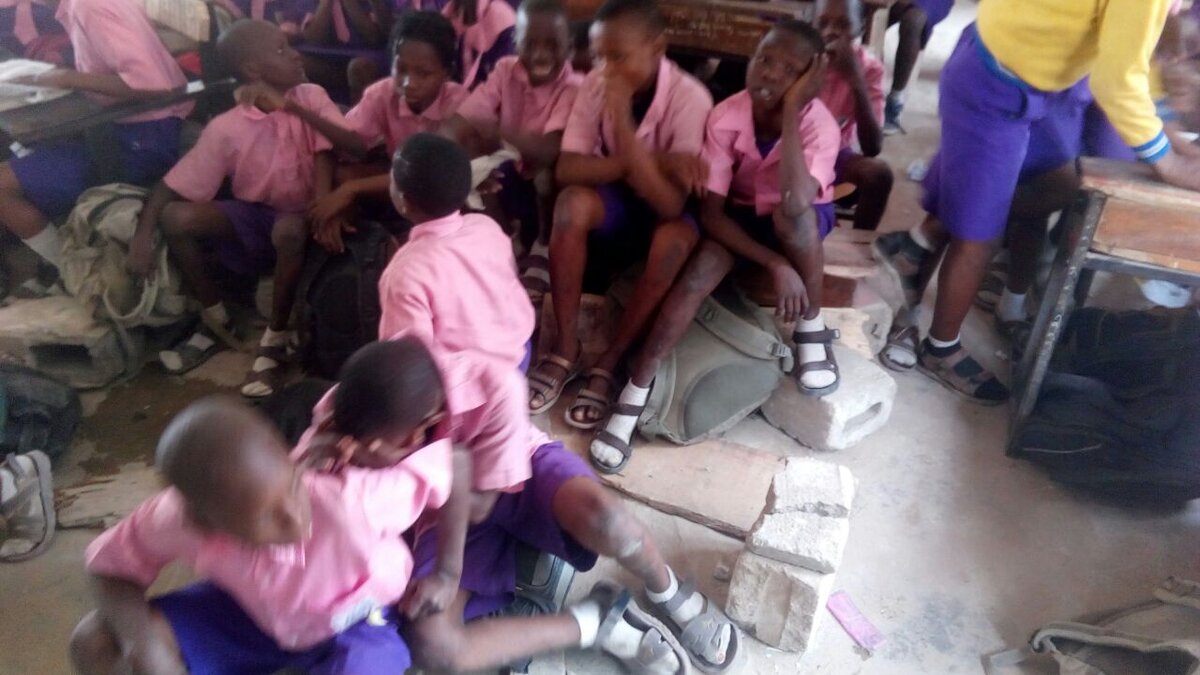 Pupils seated on blocks and the floor before SLOSA's furniture donations